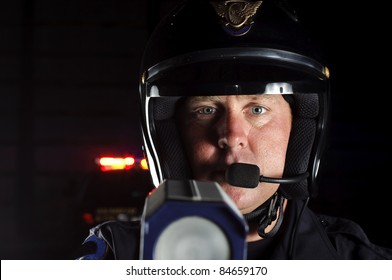 A Police Officer At Night Pointing His Radar Gun At Traffic.