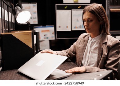 Police officer preparing to leave job after working overtime at missing person case in evidence room. Private detective analyzing crime scene report, searching for new clues. Criminology report - Powered by Shutterstock