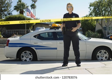 Police Officer Standing Behind Yellow Caution Tape By Car