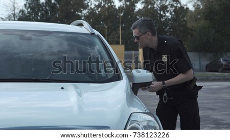 Police officer stopping the driver of a vehicle and questioning him over an alleged offence through the open window of the car