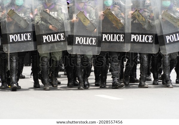Police officer team with weapons and riot\
shield protection. Violence Against Demonstrators and protesters\
during COVID-19 pandemic. Riot in Bangkok, Thailand. Demonstration\
people. Cop authority.