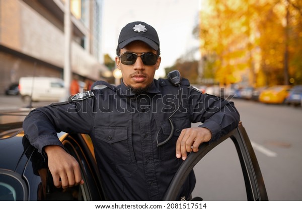 Police officer\
in uniform poses at the patrol\
car