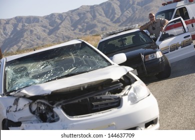 Police Officer Using Radio In Front Of A Damaged Car On Desert Road