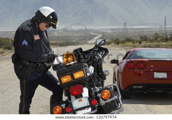 Police officer writing ticket by bike with car\
in the background