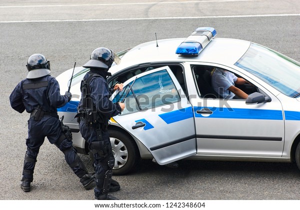 Police officers arresting criminal,\
putting him on car trunk and reading rights for\
him.\
