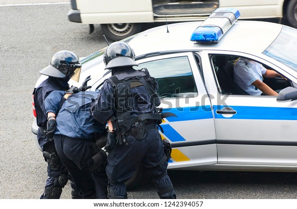Police officers arresting criminal,\
putting him on car trunk and reading rights for\
him.\
