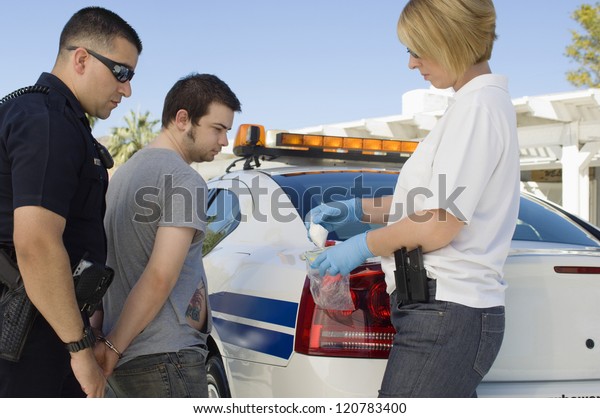 Police\
officers arresting drog dealer by police\
car