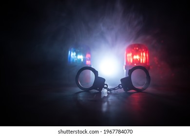 Police raid at night and you are under arrest concept. Silhouette of handcuffs with police car on backside. Image with the flashing red and blue police lights at foggy background. Selective focus - Powered by Shutterstock