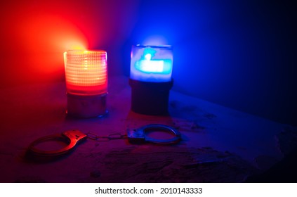 Police Raid At Night And You Are Under Arrest Concept. Silhouette Of Handcuffs With Flashing Red And Blue Police Lights At Foggy Background. Selective Focus