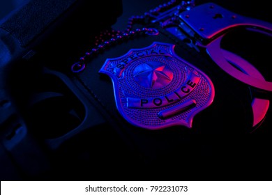 Police Raid At Night And You Are Under Arrest Concept With A Police Badge, Gun And A Pair Of Handcuffs At Night Illuminated By The Flashing Red And Blue Police Lights