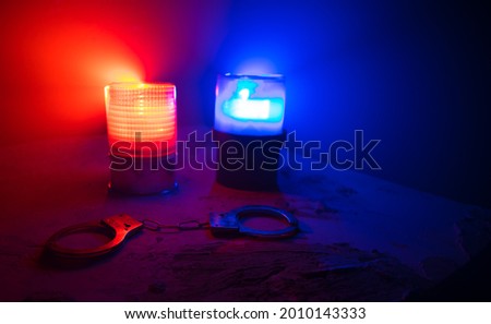 Police raid at night and you are under arrest concept. Silhouette of handcuffs with flashing red and blue police lights at foggy background. Selective focus