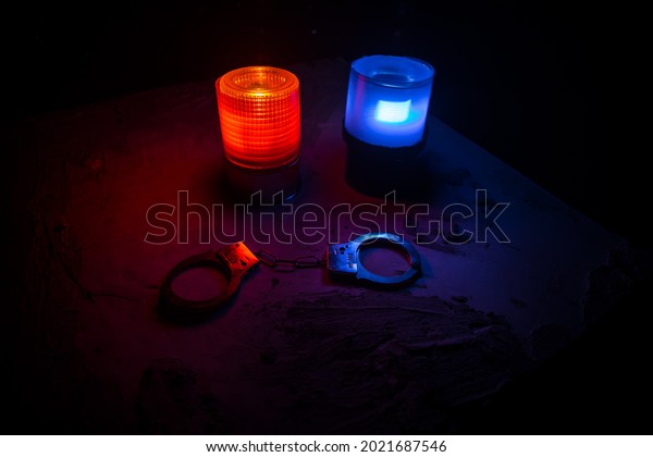 Police raid at night and you\
are under arrest concept. Silhouette of handcuffs with flashing red\
and blue police lights at foggy background. Selective\
focus