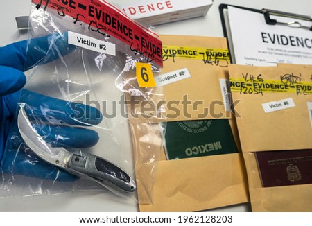 Police scientist holds evidence bag with knife evidence from a murder case next to several passports, conceptual image