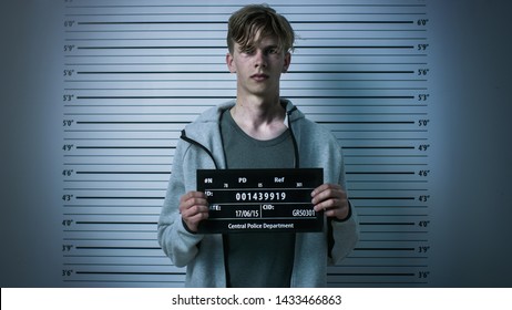In a Police Station Arrested Drug Addict Teenage Posing for a Front View Mugshot. He is Heavily Bruised. Height Chart in the Background.