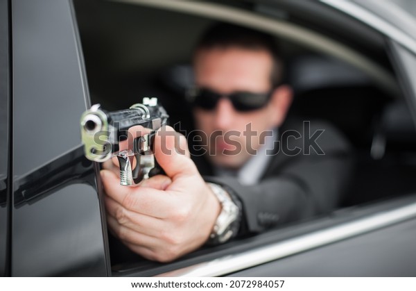 Police tactical car shooting training. Male spy\
agent bodyguard shooting from limousine. Security police in\
civilian black suit in\
action