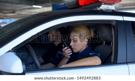 Police woman receiving call on car radio about accident, patrolling with mate
