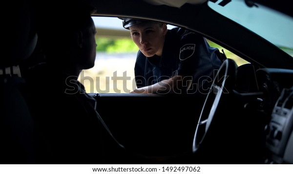 Police woman talking with driver in car,\
inspection on road, traffic\
offence