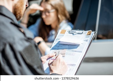 Policeman Issuing A Fine For Violating The Traffic Rules To A Young Woman Driver, Close-up View Focused On The Folder