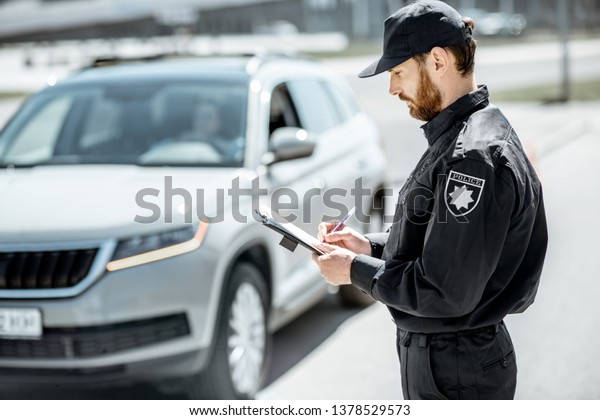 Policeman issuing a fine for\
violating the traffic rules standing in front of the car on the\
roadside