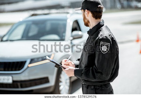 Policeman issuing a fine for\
violating the traffic rules standing in front of the car on the\
roadside