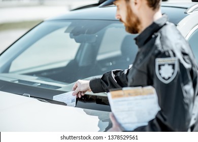 Policeman putting fine for improper parking on the windshield of the car on the roadside