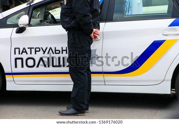 A policeman stands near a\
patrol police car with the inscription in Ukrainian Patrol Police,\
Dnepropetrovsk, Dnipro city. Ukraine police, policeman\
Ukraine