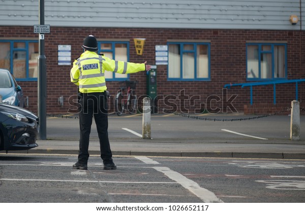 policeman wearing helmet and hi vis reflective\
jacket directs traffic on busy\
road