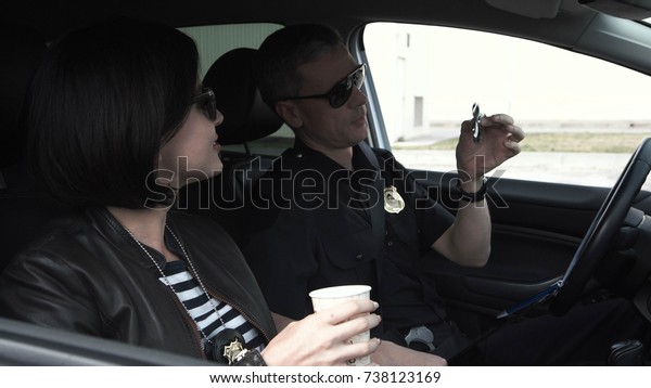 Policemen sitting in car, talking with\
each other and drinking coffee while being on\
mission.