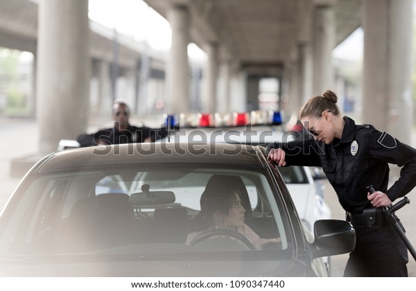 policewoman in sunglasses\
talking to woman sitting in car and policeman standing behind near\
car 