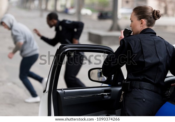 policewoman talking by radio set while her partner\
chasing thief