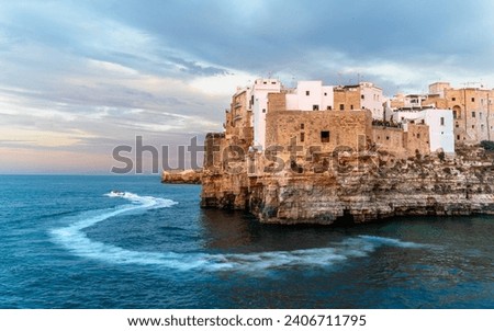 Polignano a Mare , Italy. The oldest part of the town stands on a rocky spur overlooking the Adriatic Sea while motor boat passing by leaving white trace on a blue water. 