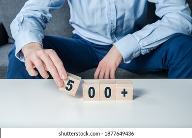 Polish Family Support System 500+, Social System. The Man Holds Wooden Blocks With The Word 500+ In His Hands, Adding The Cube 5.