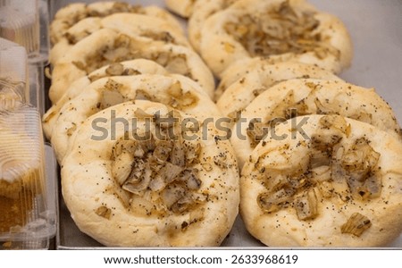 Polish flatbread buns with crispy fried onions on top, displayed on a bakery counter. Golden brown crust, savory aroma, popular traditional street food in Poland.