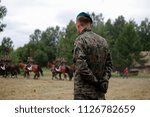 The Polish military man in a green beret is standing with his back behind his back. Against the backdrop of a soldier, the Polish cavalry.