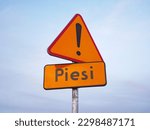 A Polish yellow warning road sign "Piesi" informing about pedestrians in the area, low angle view on clean clouds background