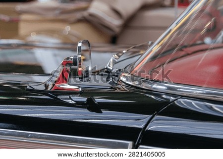 A polished chrome side mirror is mounted on a black vintage convertible automobile. Reflections and chrome accents emphasize classic automotive design.
