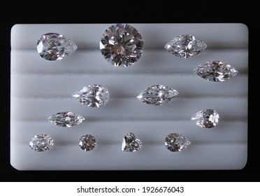 Polished diamonds of different cuts and sizes sorted on white platform to evaluate the color of diamonds. Top view close up.