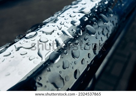 A polished stainless steel handrail is photographed close-up, it has been raining and many drops are shining on the surface of the metal, an abstract photo