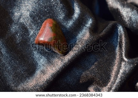 Polished unakite on shiny draped fabric.Scarlet olive green mineral on day light, a closeup.Textured semiprecious stone.Geology, mineralogy, healing concept, jewelry material, litho therapy.