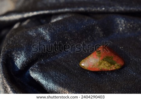 Polished unakite on shiny draped fabric.Scarlet olive green mineral on day light, a closeup.Textured stone.Geology, mineralogy, healing concept, jewelry material, litho therapy.