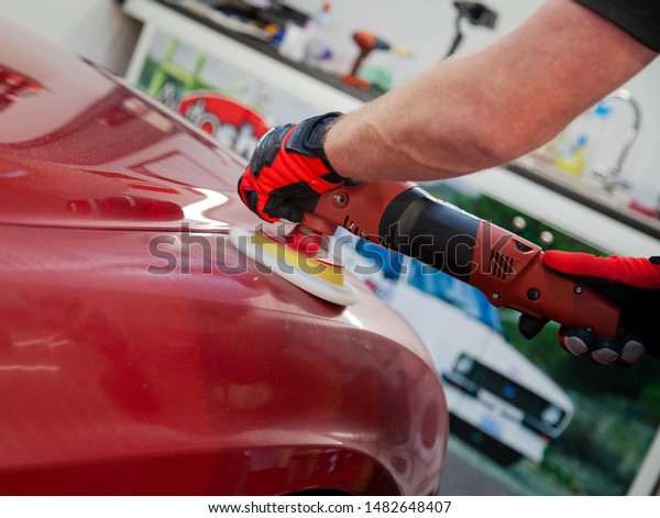 Polishing a red car with\
handheld polisher