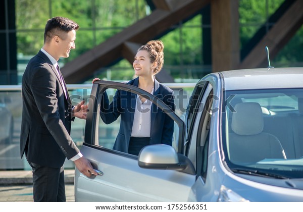 Polite behavior. Polite young man\
in a suit opening a car door for a pretty smiling\
woman.