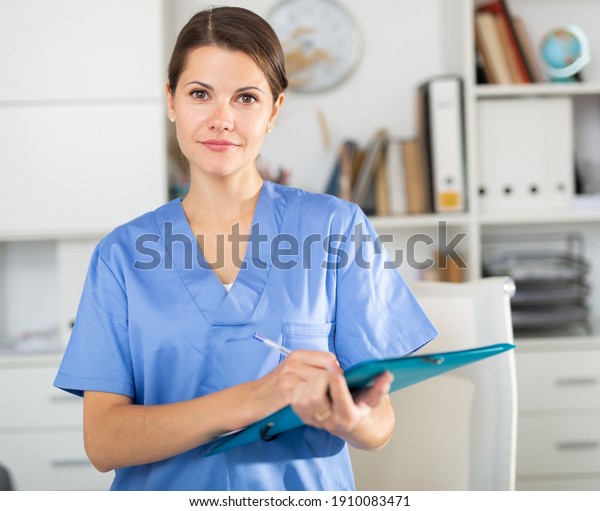 Polite female doctor meeting\
patients in medical office, filling out medical form on\
clipboard