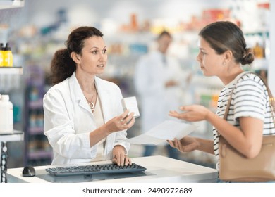 Polite middle-aged female pharmacist consulting young girl about medicament in box according to her recipe in chemist's shop - Powered by Shutterstock