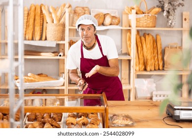 Polite middle-aged salesman holding a service clip while ready to assist customers in bakery - Powered by Shutterstock