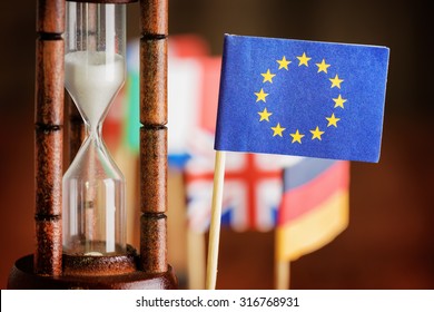 Political concept with flag of the European Union (EU). Time is running out. Closeup view of hourglass and flag of the European Union (EU). Flags of European countries in background.