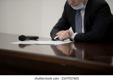 Politician With Clasped Hands Sitting Behind Desk.