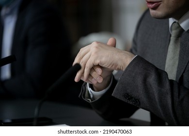 Politician With Clasped Hands Sitting Behind Desk.