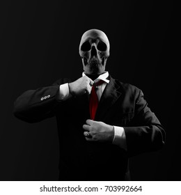 Politician With Skull. Black And White Politician Man With Skull Head In Black Suit Straightens A Red Tie On Black Background.