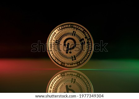 Polkadot DOT cryptocurrency physical coin placed on reflective surface and lit with green and red lights